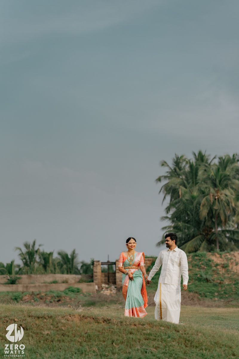 Indian wedding couple holding hands walking through green fields with palm trees.