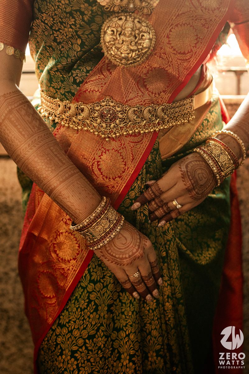 Close-up of South Indian bride in green Kanjivaram saree with gold vaddanam belt and mehndi bangles.