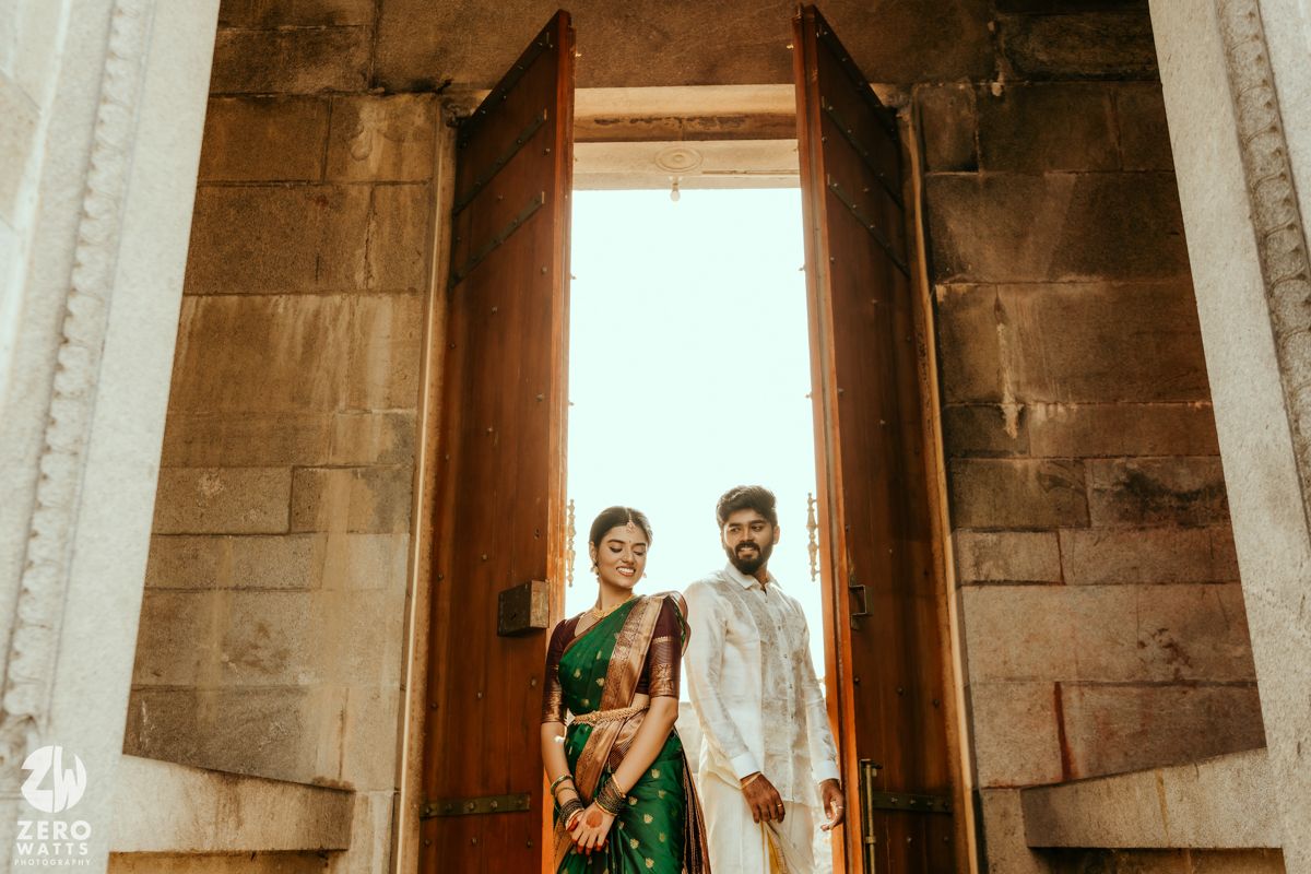 South Indian wedding couple in traditional attire posing together at ancient stone temple wooden doors.