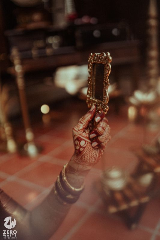 A henna-adorned hand holds an ornate gold mirror at a traditional Indian wedding ceremony.