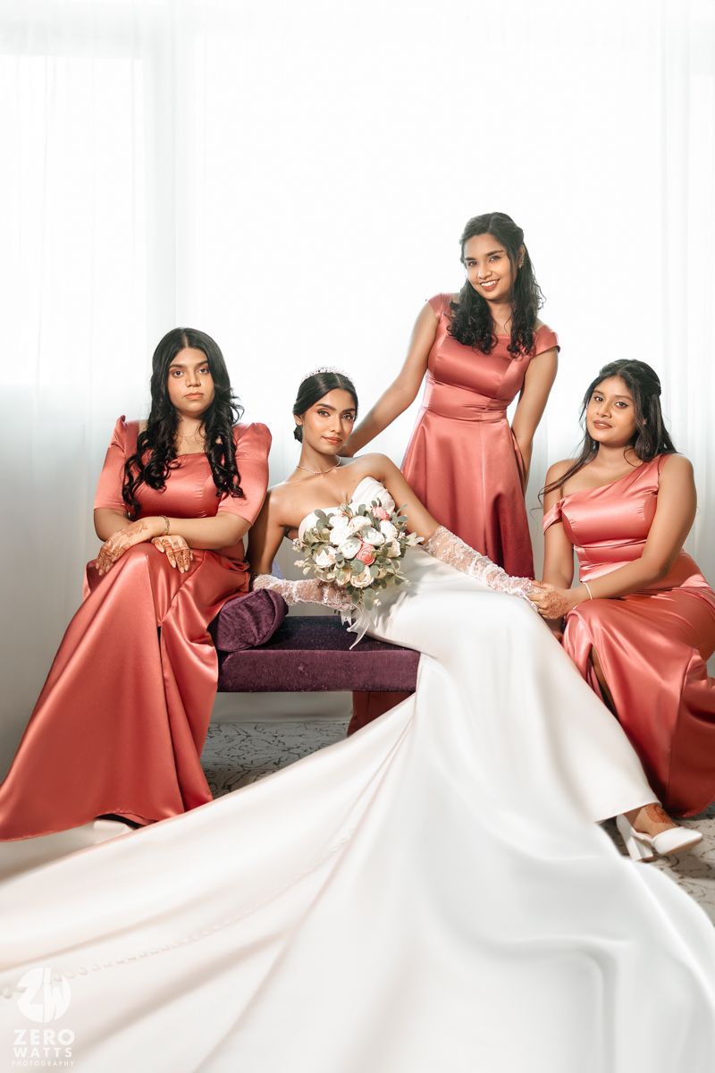 Bride in white gown with three bridesmaids in coral satin dresses posing for a portrait.