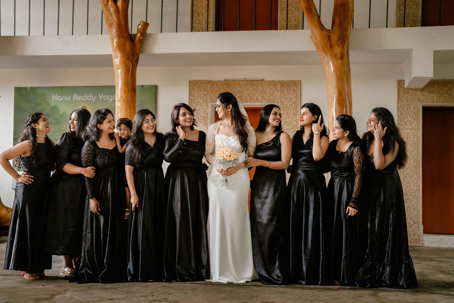 Wedding party poses together with bride in white gown surrounded by bridesmaids wearing elegant black dresses.