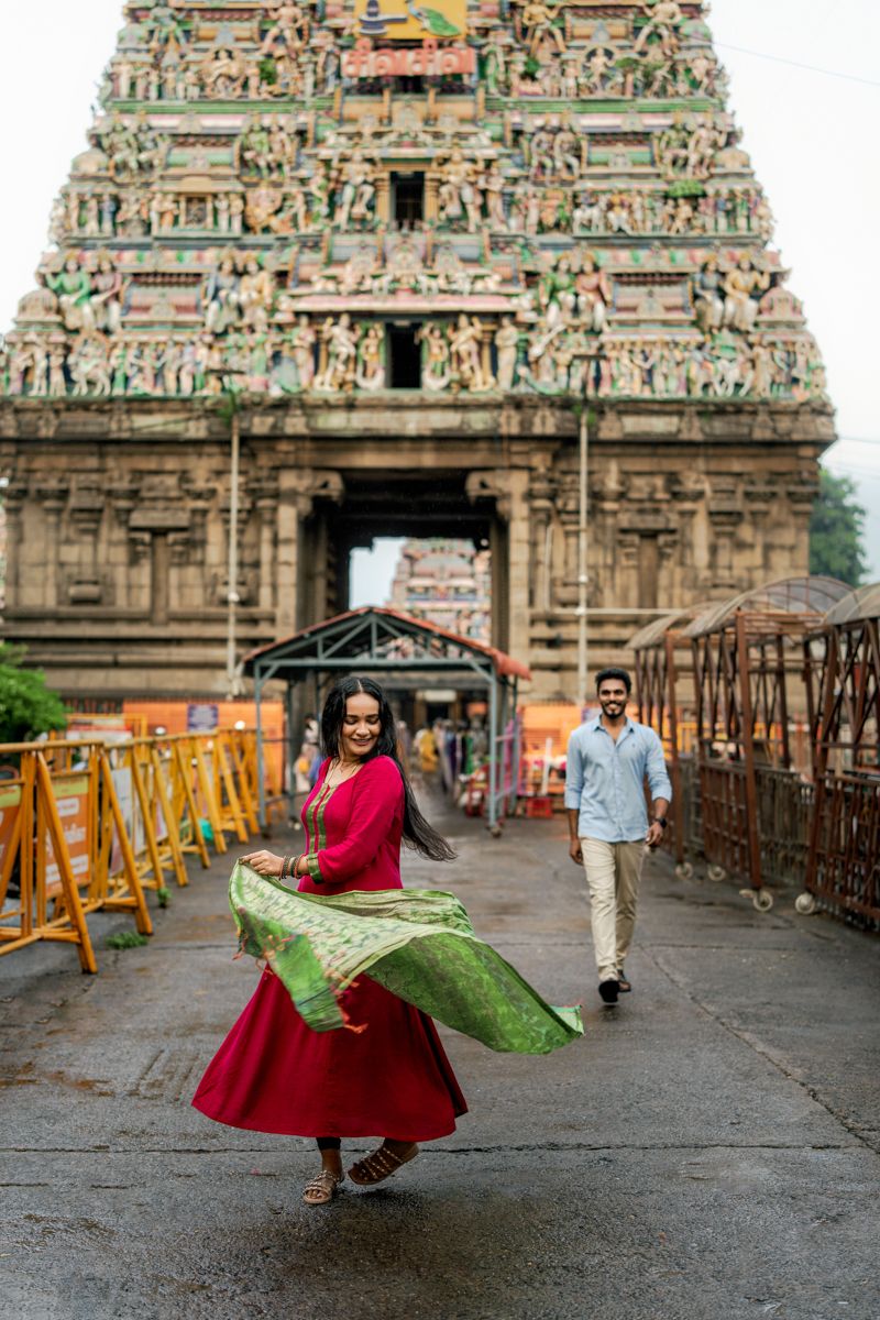 A person in a red dress twirls joyfully in front of an ornate South Indian temple with intricate stone carvings.