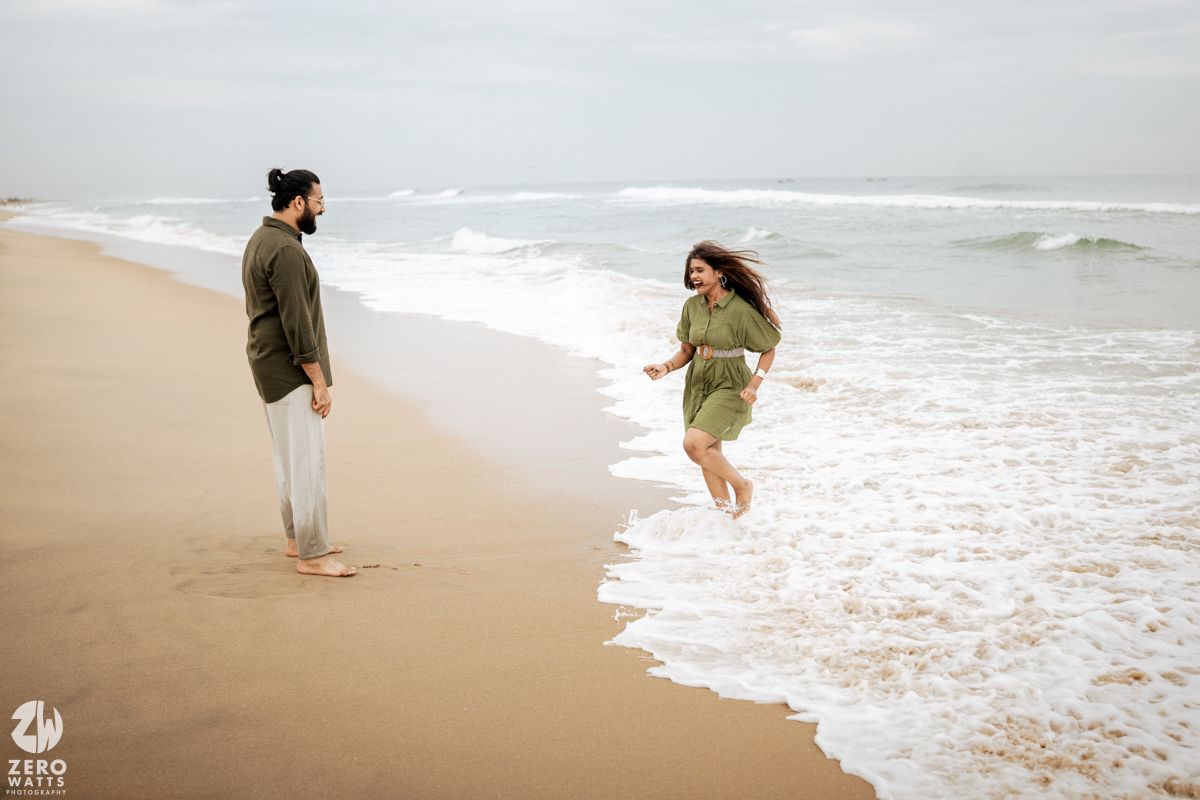 Couple enjoying a romantic moment while walking along a misty beach shoreline at sunset.