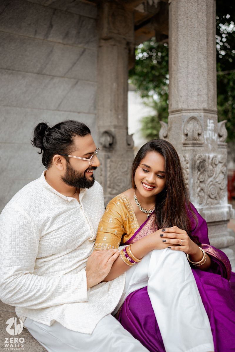 Couple in traditional Indian attire share a tender moment under stone architecture.
