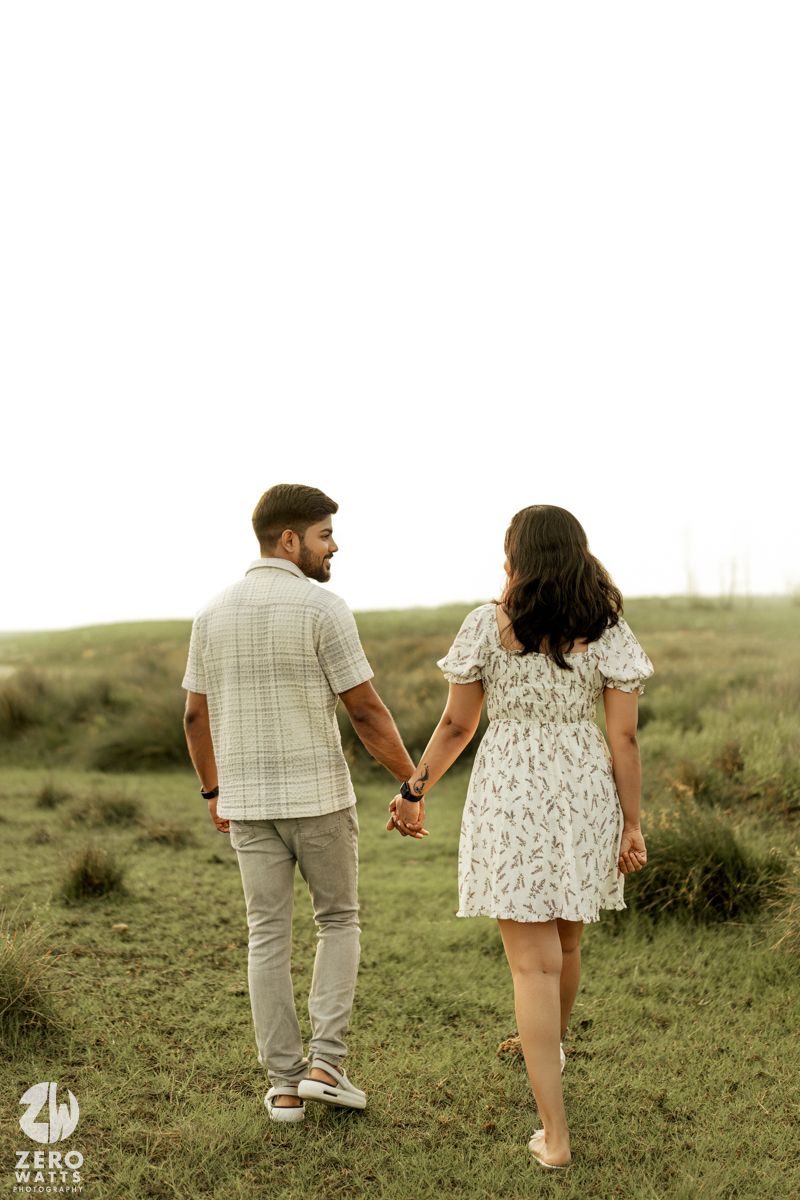 A couple holding hands while walking together on a grassy hillside in casual attire during a romantic moment.