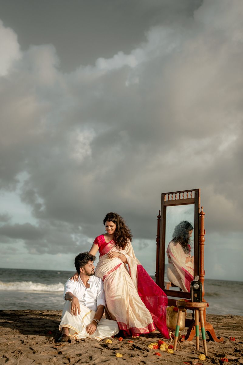Dramatic beachside portrait session with wooden mirror frame and floral decorations under stormy skies.