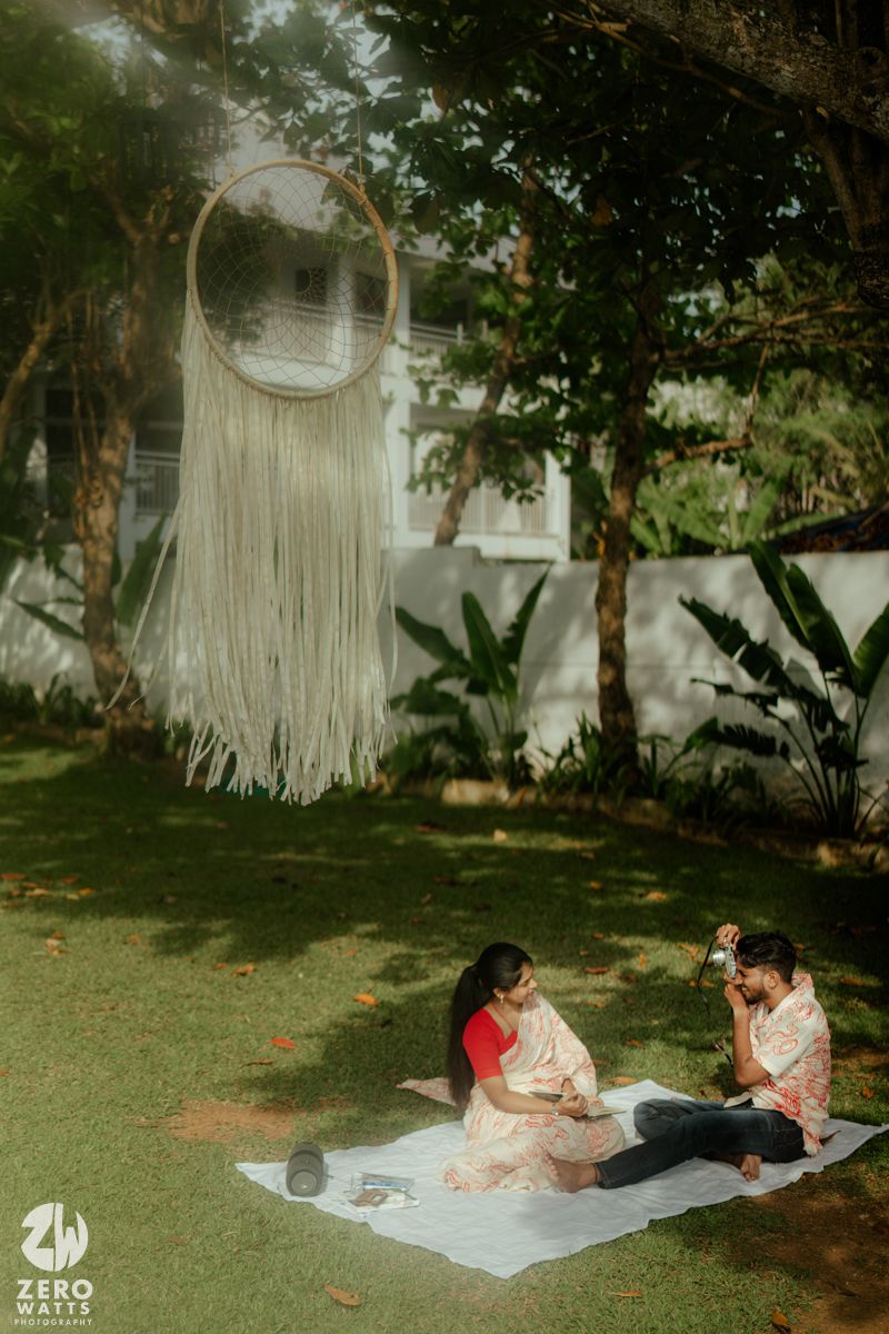 Couple relaxing on white blanket in garden setting with macrame decorations and natural lighting.