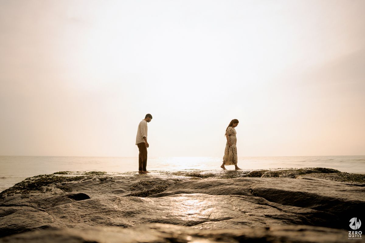 Panoramic sepia view of two figures standing on rocky coastline during sunset.