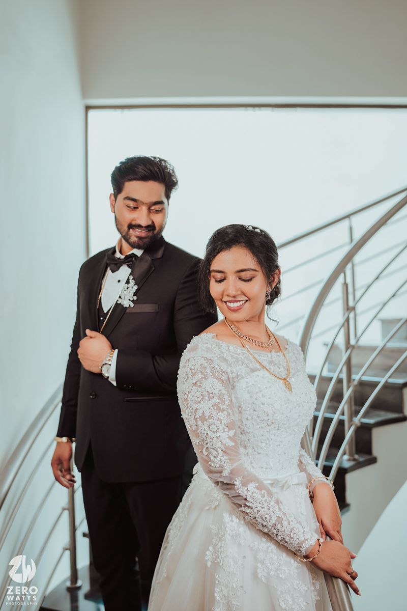 Wedding couple in formal attire pose together on modern staircase with metal railings.