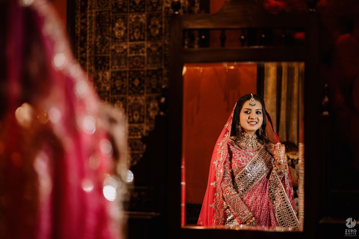 A person in an ornate red and gold Indian wedding lehenga poses elegantly during a traditional ceremony.