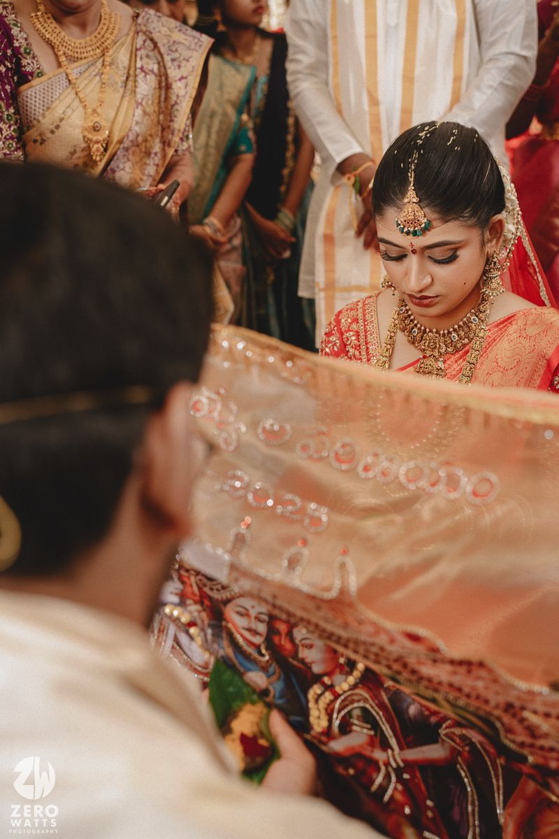Traditional Indian wedding ceremony showing intricate details of bridal jewelry and red sari during a ritual moment.