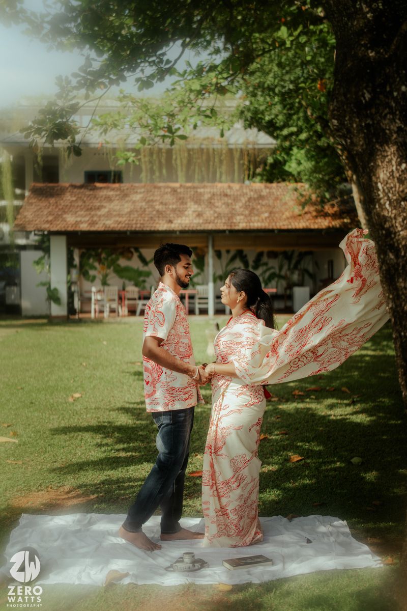 A couple dances playfully outdoors in a garden setting with flowing red and white fabric creating graceful movements.