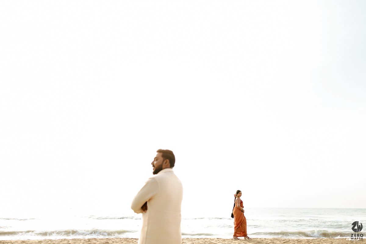 People walking on a sandy beach at sunset with silhouettes against an orange sky and ocean waves.