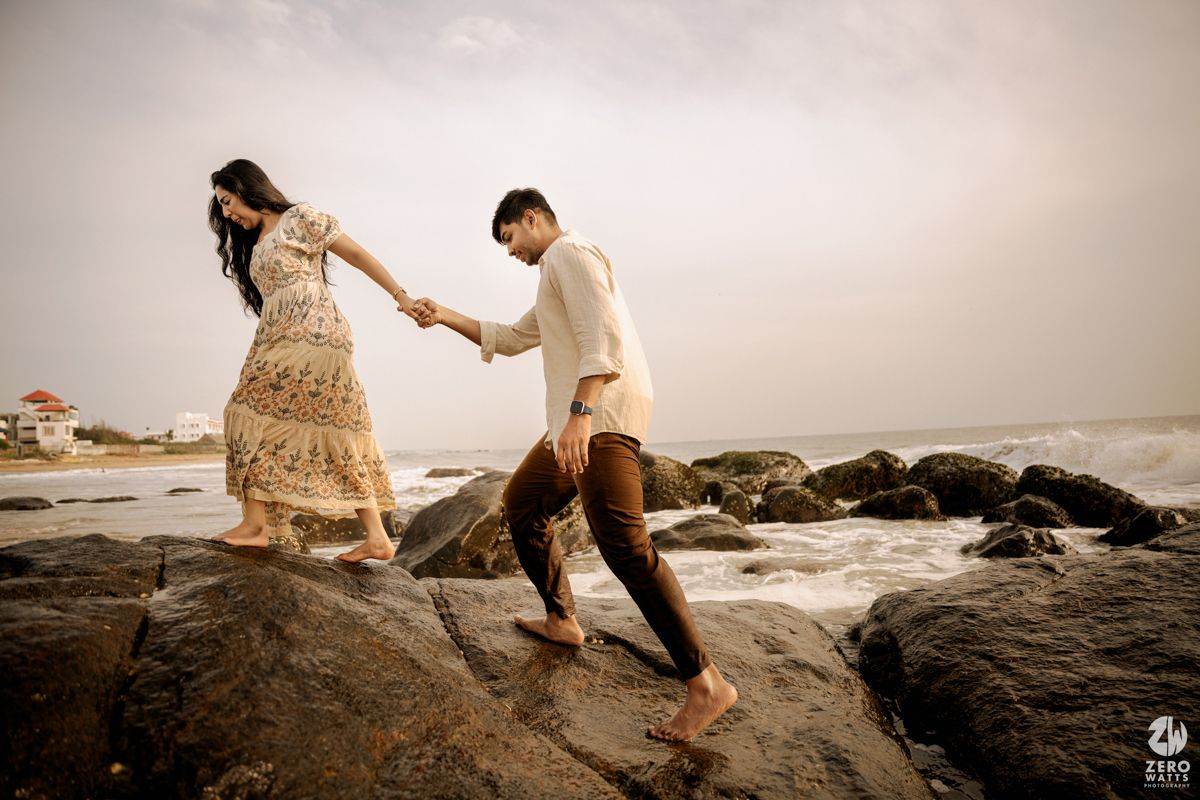 A couple walking and playing along rocky coastal cliffs at sunset.