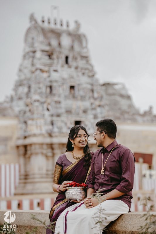 A romantic couple in traditional Indian attire share tender moments against a temple backdrop with ornate architecture.