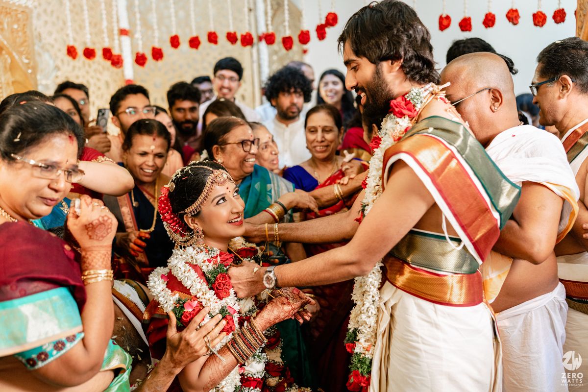 Joyful South Indian wedding ritual with bride and groom exchanging garlands surrounded by smiling family members in traditional attire.