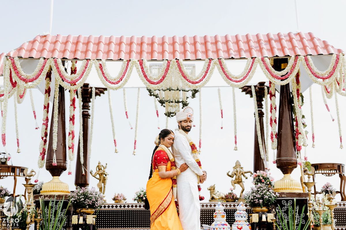 South Indian wedding couple standing under decorated mandap with floral garlands.