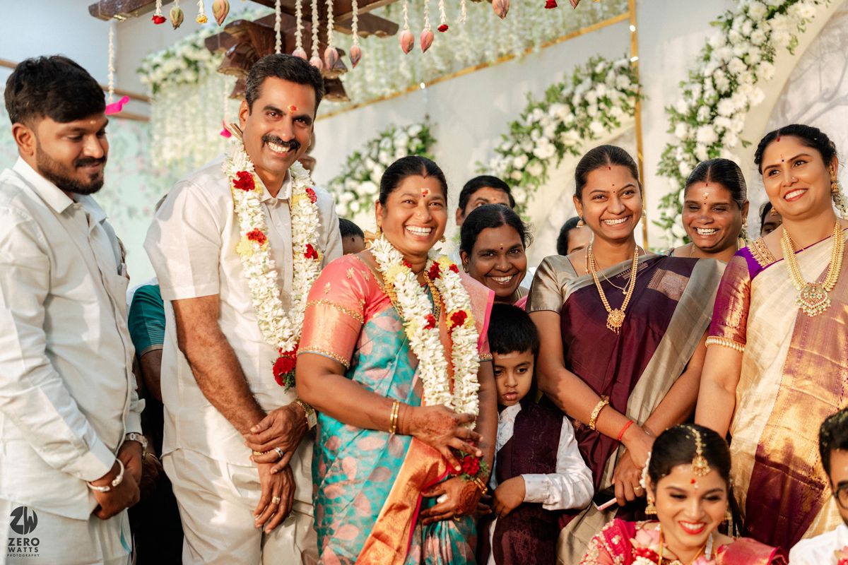 Joyful South Indian wedding family portrait with bride, groom in traditional attire and flower garlands.