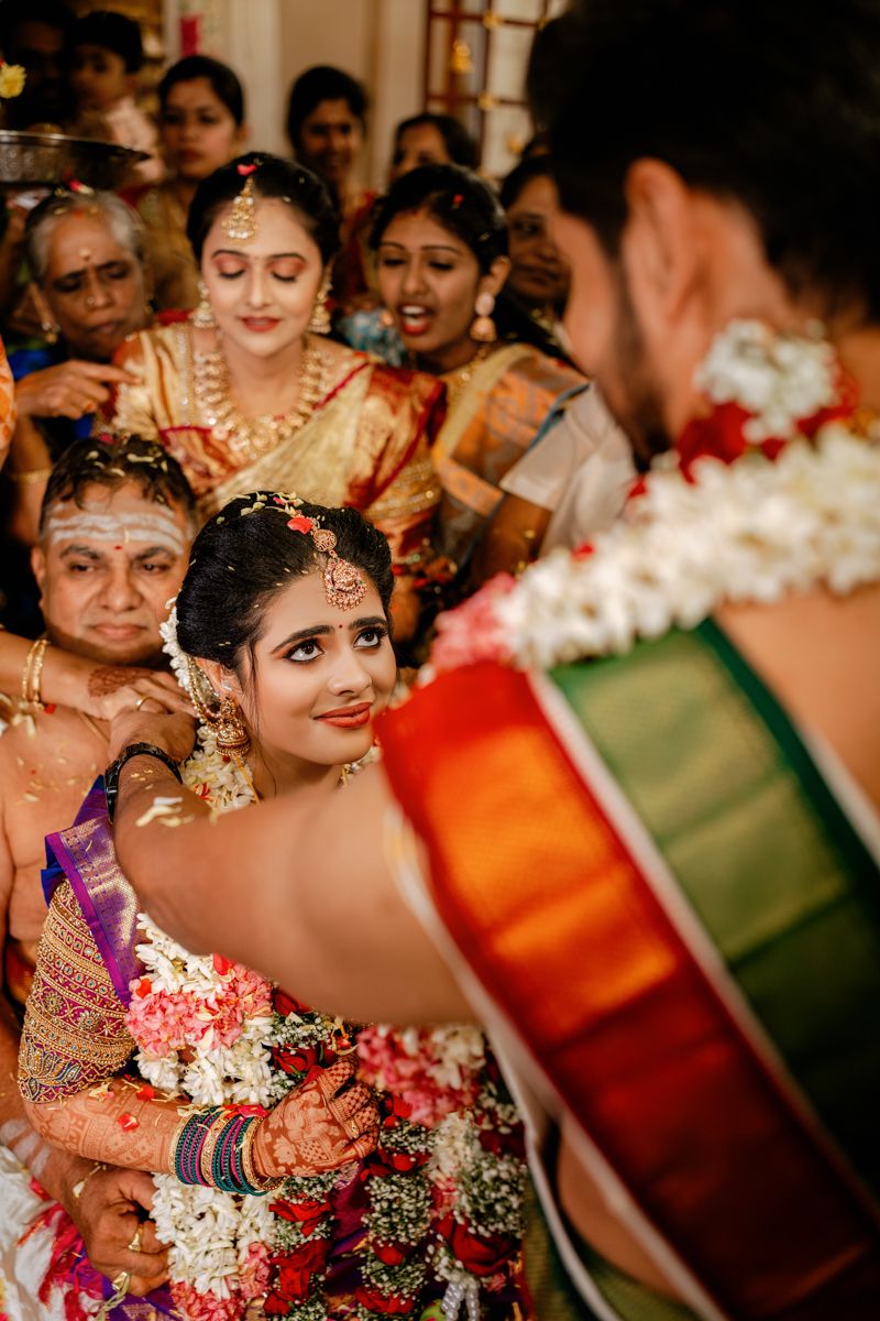 Traditional Indian wedding ceremony with vibrant orange and green attire and floral garlands during an intimate celebration.