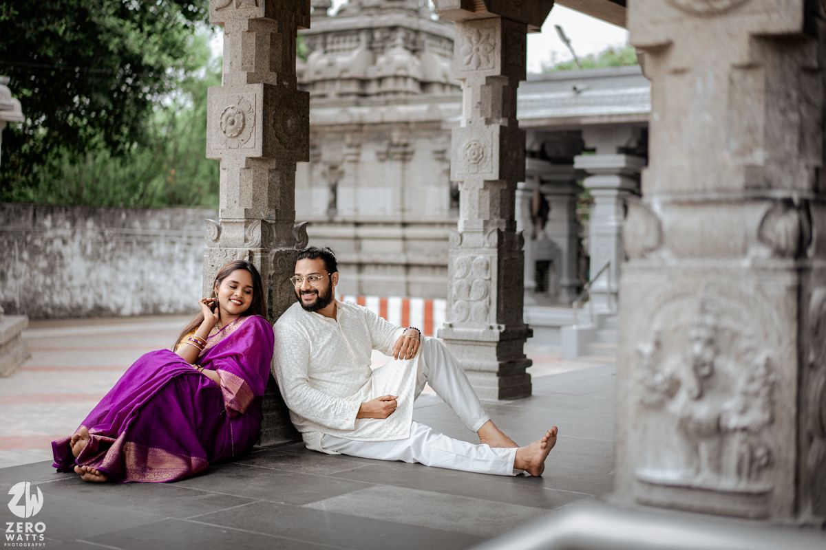A couple in traditional Indian attire sits together in a stone temple corridor during a romantic photoshoot.