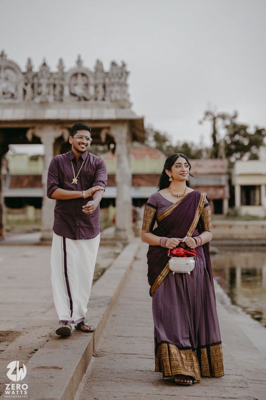 Couple in traditional South Indian attire poses together at a temple complex with ornate architecture in the background.