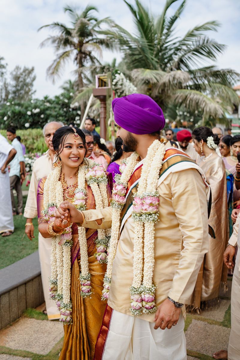 Outdoor Indian wedding ceremony with palm trees and guests in traditional attire on a beachfront setting.