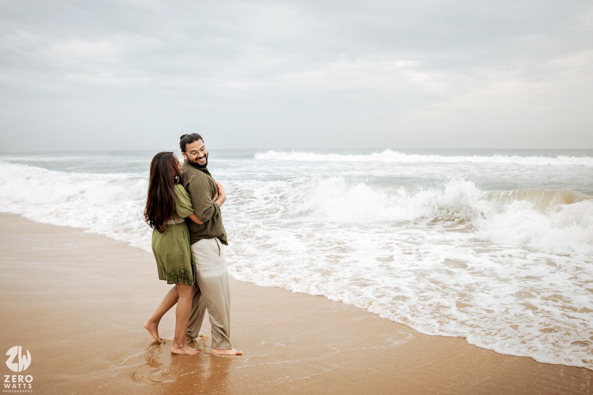 Couple playing and splashing in the ocean waves at a cloudy beach.