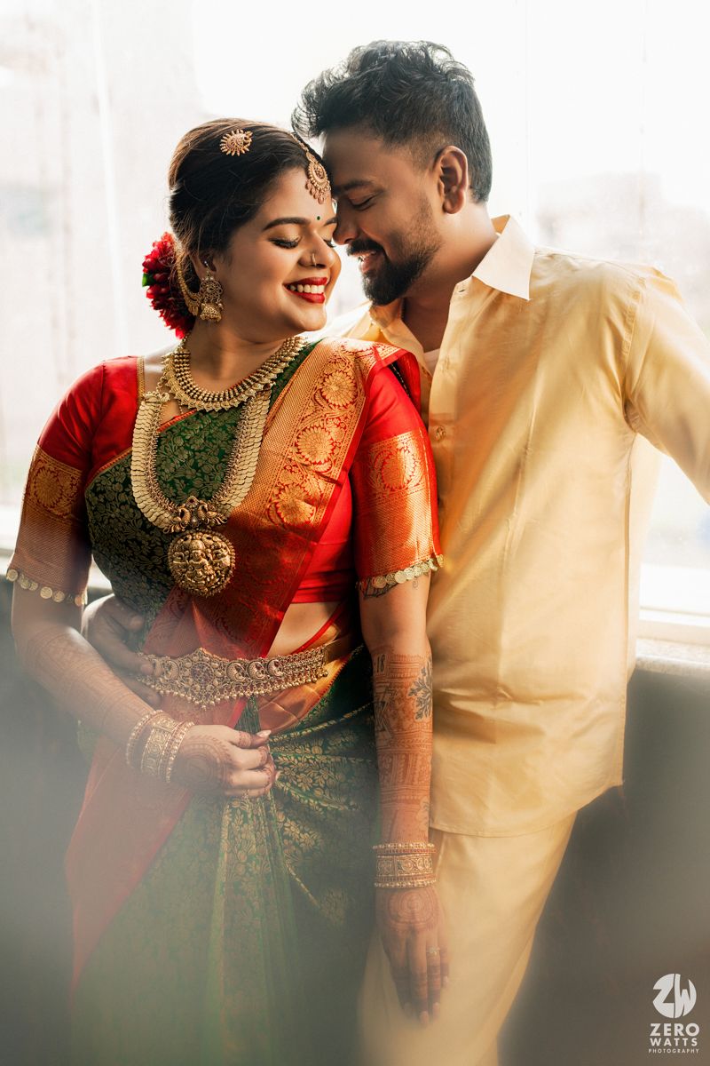 South Indian bride and groom sharing a joyful moment in traditional wedding attire with gold jewelry.
