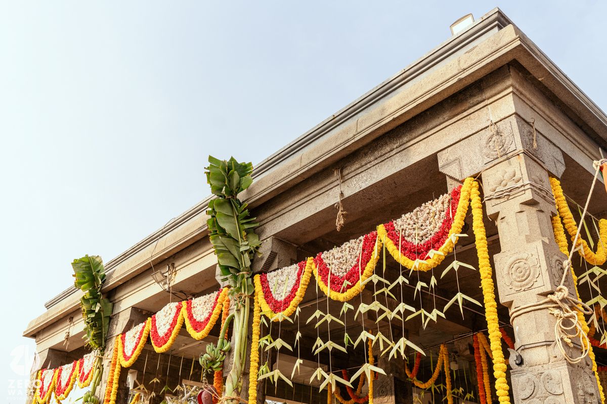 Colorful flower garlands and banana leaves decorate a stone temple entrance during a festive Indian celebration.