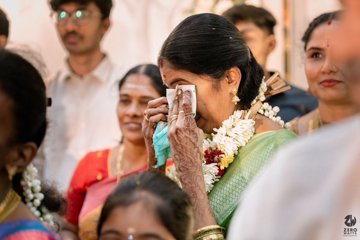 Emotional mother wiping tears at a South Indian wedding ceremony surrounded by guests.