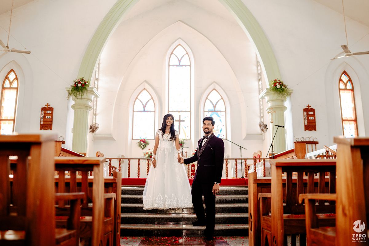 Newlywed couple holds hands at church altar, bride in white gown and groom in dark suit, surrounded by elegant decor.