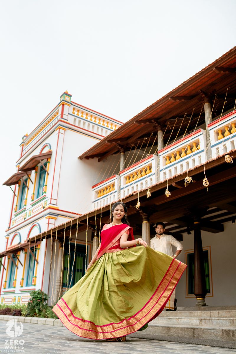 Bride twirling in a green and red lehenga outside a colorfully decorated traditional South Indian mansion.
