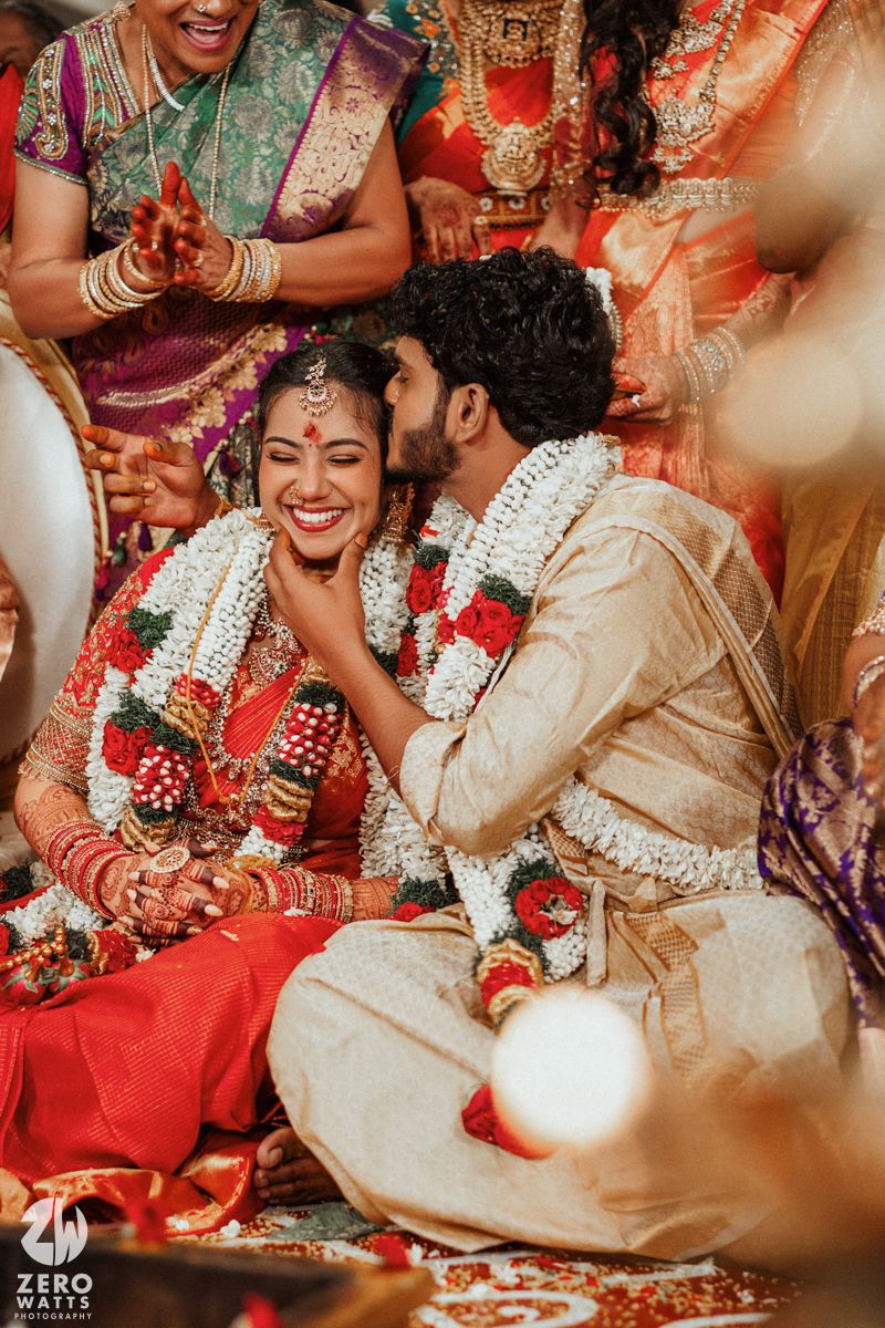 Joyful South Indian couple exchange garlands during traditional Hindu wedding ceremony surrounded by family in colorful sarees.