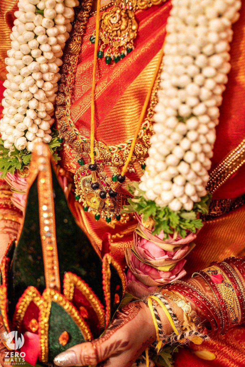 Close-up of South Indian bride wearing gold temple jewelry and white jasmine garland with red silk saree details.
