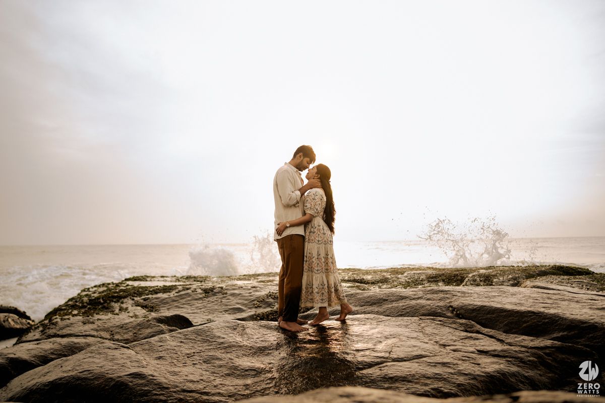 Silhouetted figures stand together on a rocky cliff overlooking a misty coastal landscape at sunset.