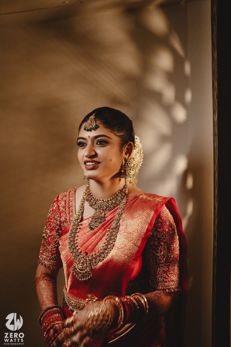 Traditional Indian bride in red silk saree and ornate gold jewelry poses elegantly in dramatic lighting.
