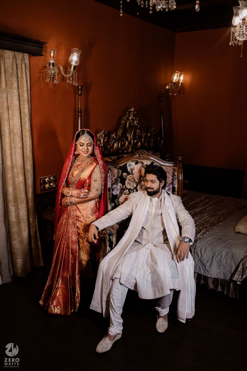 A couple in traditional wedding attire pose in an elegantly lit room with chandeliers.