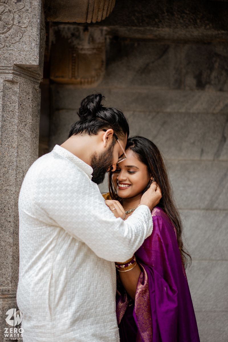 A romantic couple moment captured between stone pillars with white and purple traditional outfits.