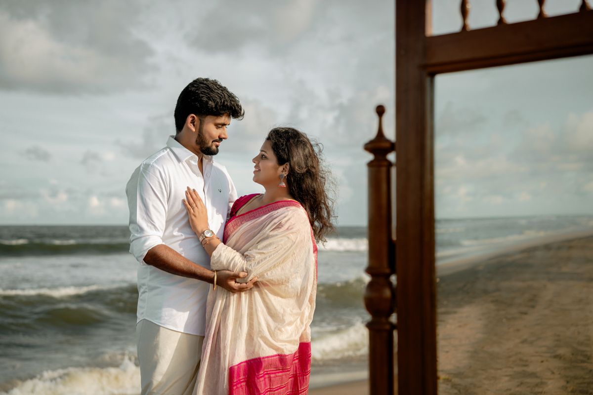 A couple enjoying a romantic beach setup with vintage decor and wooden furniture by the ocean.