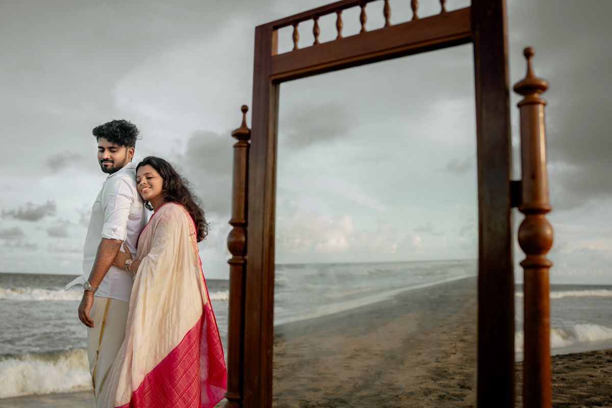 A wooden mirror frame stands on a dramatic beach landscape with moody clouds overhead.