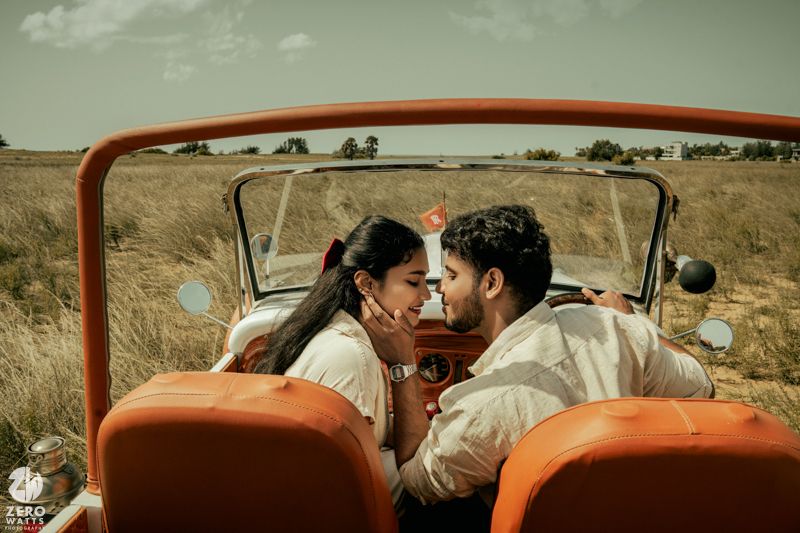 Couple enjoying a tender moment inside an orange vintage convertible car.