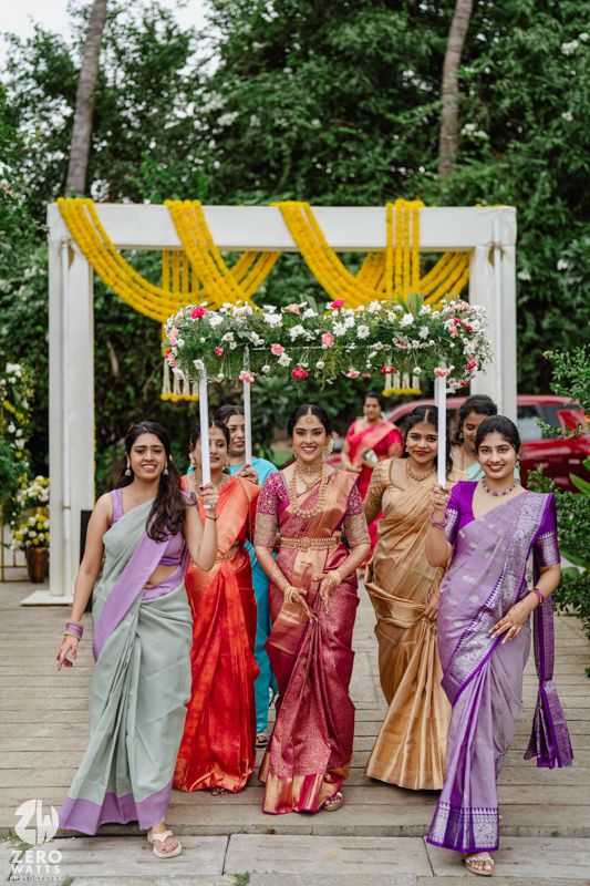 Group photo of women in colorful silk sarees posing together under a decorated outdoor wedding mandap.
