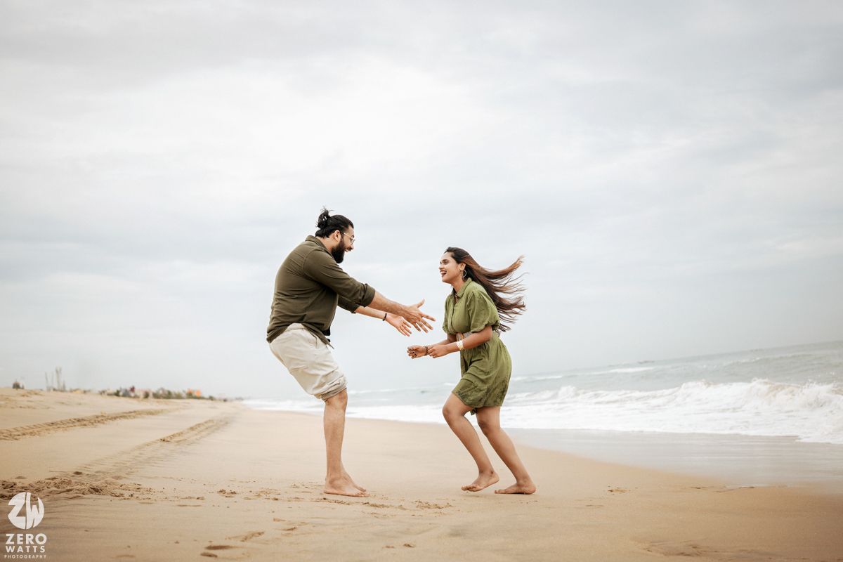Couple holding hands and dancing together on a foggy beach shoreline during overcast weather.