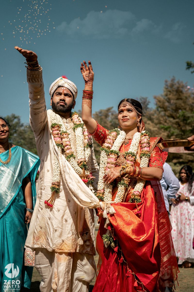 South Indian bride and groom tossing rice outdoors during traditional wedding ritual.