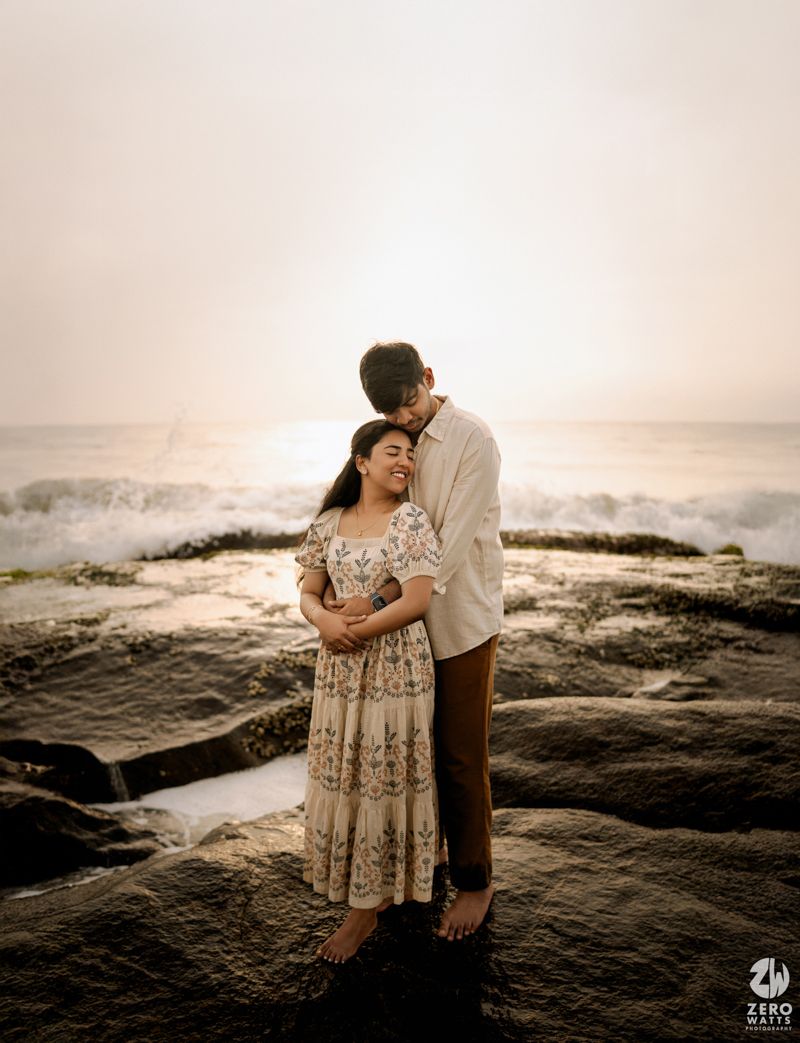 Couple shares romantic moments on rocky coastal cliffs during sunset at the beach.