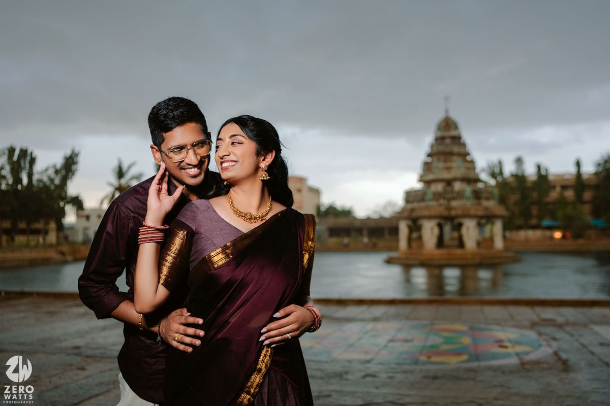 Couple embracing by serene waterfront with historic Indian temple in background at dusk.