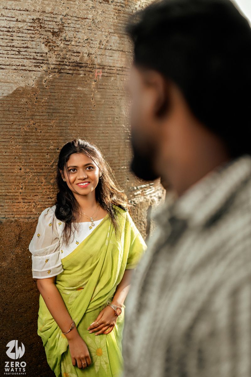 A couple poses against a textured brick wall in traditional attire during an outdoor photoshoot.