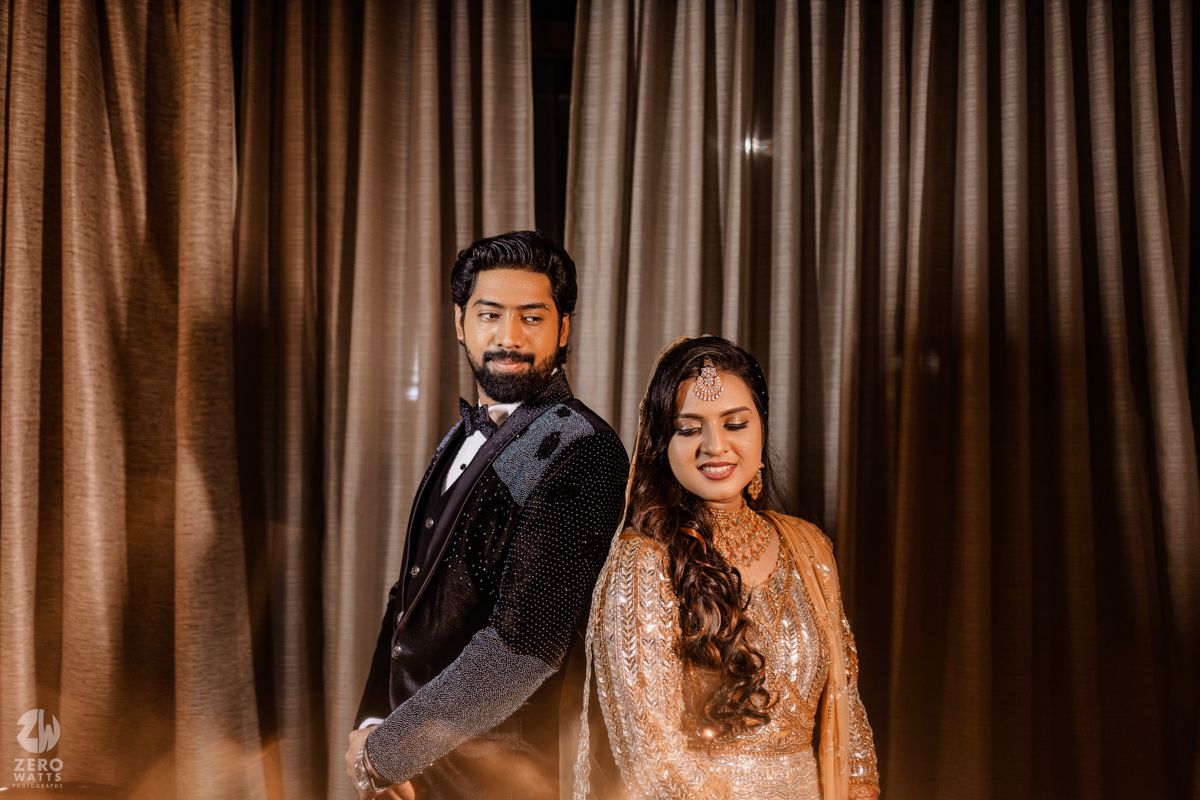 Elegant couple in formal attire pose against brown curtain backdrop during evening event.