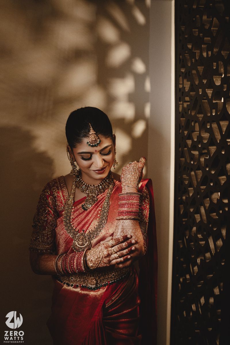 A bride in traditional Indian attire adorned with jewelry and henna showcases intricate details in a moody lighting setup.